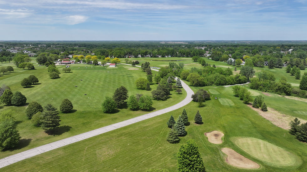 drone image of a golf course showing multiple golf holes, sand traps, trees and a cement drive leading up the club house