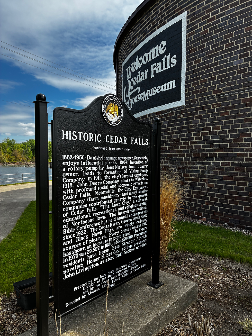 Exterior black sign that says Historic Cedar Falls in foreground and a brick circular building in background with a sign that says Welcome Cedar Falls Ice House Museum