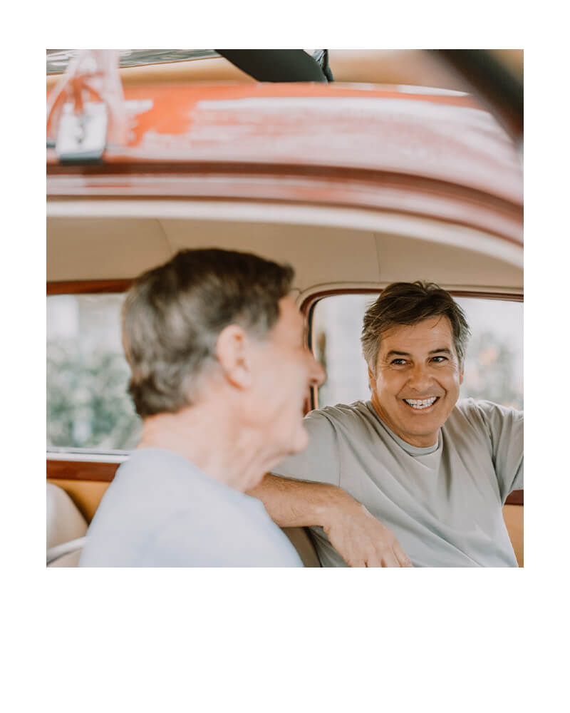 Two men smiling inside a car, enjoying their day together.