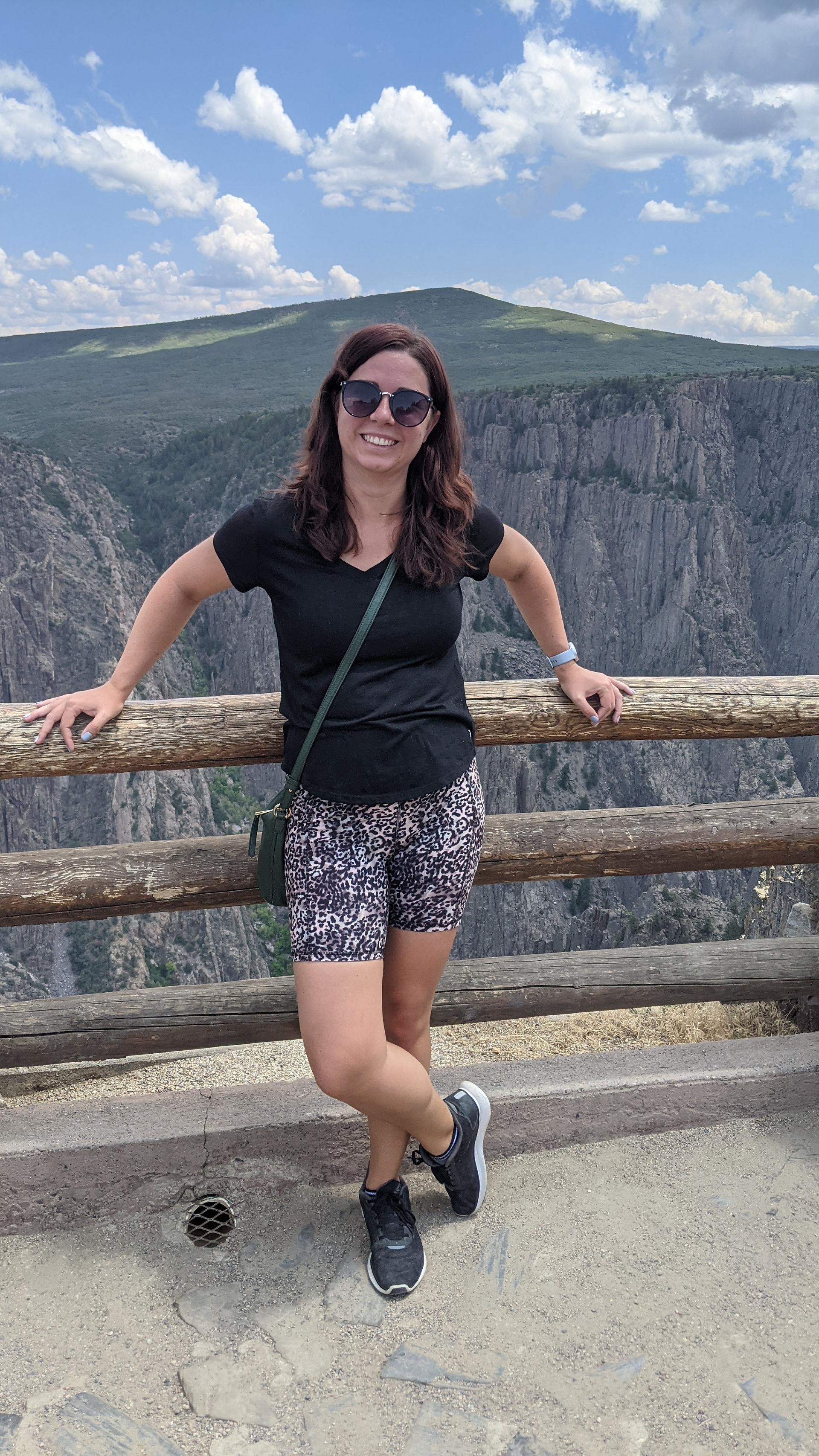 A woman poses against a wooden railing with the canyon walls behind her