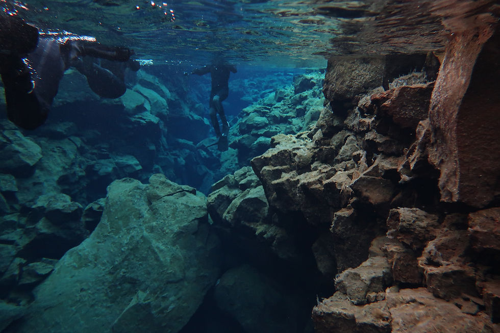 Two scuba divers swim through a rocky underwater cave with blue light filtering in, calm and exploratory mood