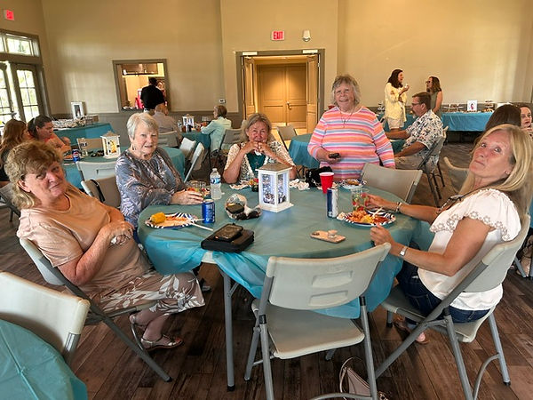 A table of older woman sit around a table and smile for the camera