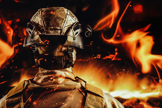 Photo of a soldier in desert olive uniform standing in helmet back view on burning fire ba