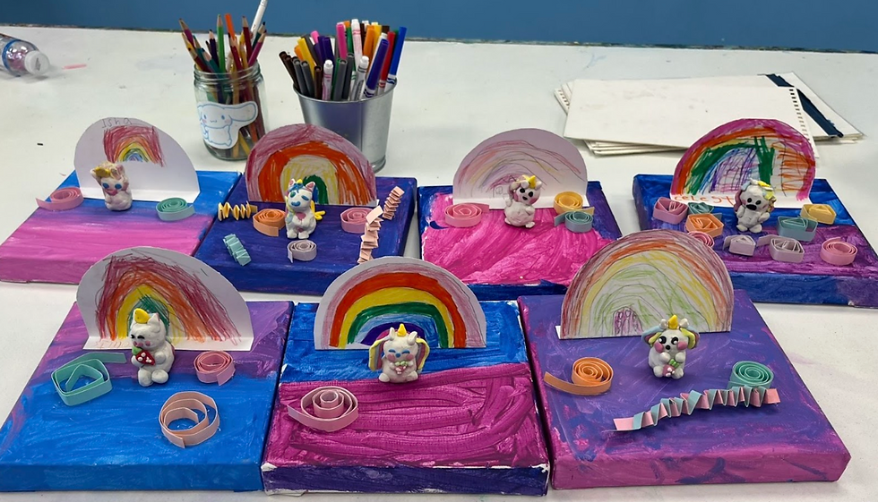 Colorful unicorn crafts with rainbows and paper spirals on painted canvases. Background includes pencil holders and scattered papers.