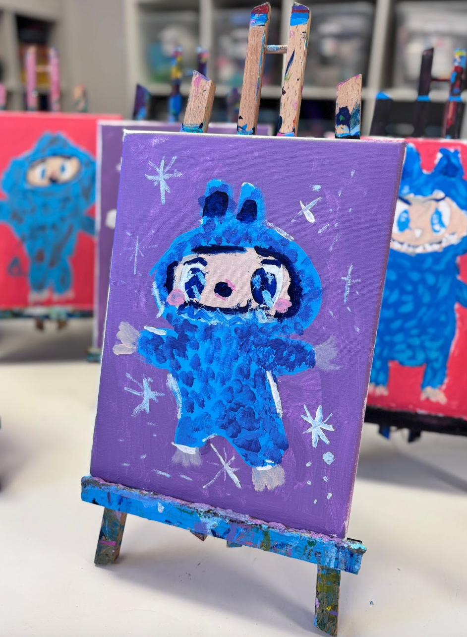 Colorful canvas on an easel shows a cute character in a blue costume on a purple background with stars. 