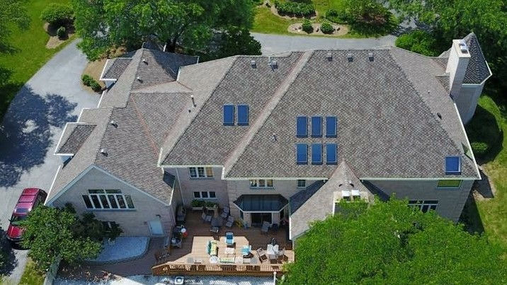 Aerial view of a large Home with multiple roofs, skylights, deck.