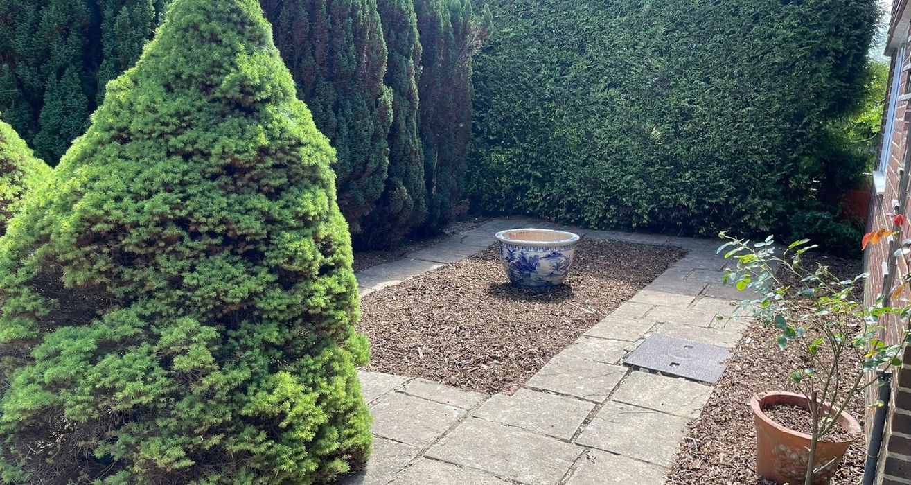 Paved patio garden featuring gravel, a decorative pot, and tall hedges.