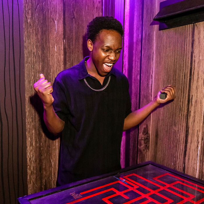 Excited man celebrates, holding object above red lit puzzle, wooden wall background.