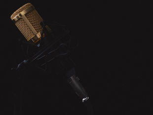 Gold condenser microphone in a black shock mount against a dark studio background