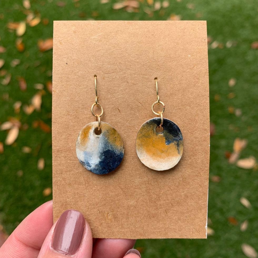 Photo of oval earrings made from seashell and paper, in blue, ochre and white, with gold.