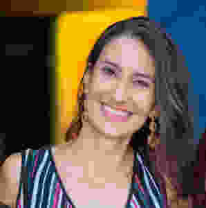 Bebel sorri para a foto, de blusa listrada colorida e brincos grandes e dourados