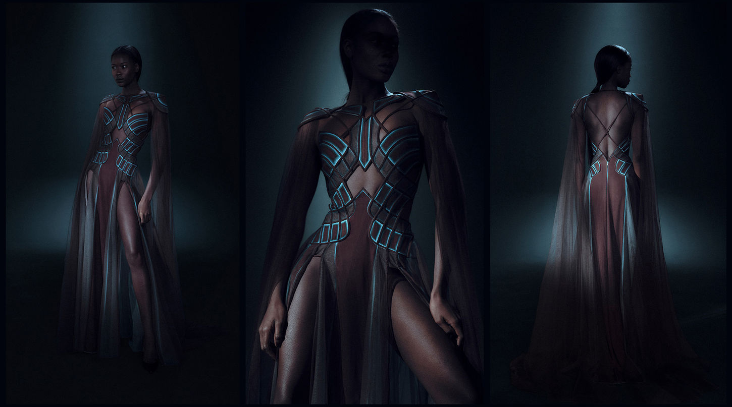 An African female model wearing a Hassidriss halter-neck crepe and tulle dress featuring a neon-like print in shades of turquoise and brown to accentuate the squared designs on the bust and hips, with two leg slits and a long sheer tulle shoulder cape.