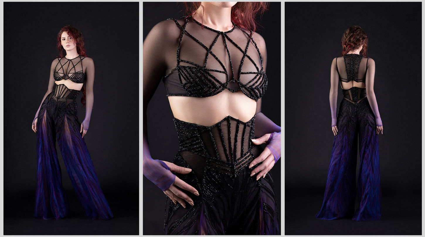 A red-headed female model is wearing a long-sleeved black beaded Hassidriss bralette and high-waisted black, purple, and blue embroidered flared trousers.