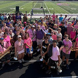 Students in pink 'BAND' shirts and instruments gathered on a field.