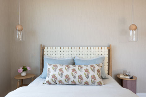 Bedroom with wooden headboard, blue pillows, and pendant lighting.