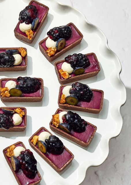 Blueberry-topped mini desserts arranged neatly on white plate.