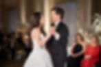 A couple dances, smiling, in formal attire at a wedding reception with guests seated in the background, soft lighting, and floral décor. Adolphus Hotel Dallas