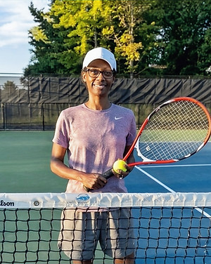 Jamica is standing on a tennis court at the net holding a tennis racket and a tennis ball