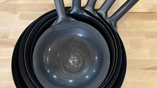Five nested black carbon steel wok on a wooden table, handles aligned upright.