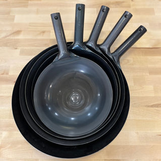 Five nested black carbon steel wok on a wooden table, handles aligned upright.