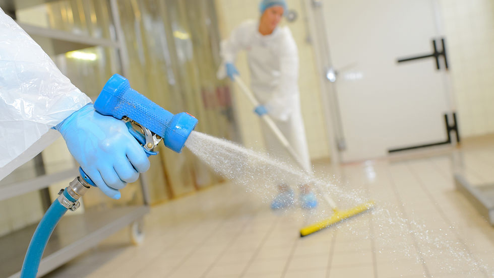 Close-up view of a person's hand using a high-pressure washer pipe, meticulously cleaning the floor of a pharmaceutical manufacturing plant