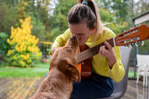 Woman playing guitar while comforting her dog outdoors.