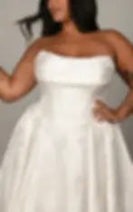 An elegant plus-size bride posing in a luxury white ballgown wedding dress. The gown showcases an impeccably structured bodice with a dramatic V-shaped basque waist that flows seamlessly into a voluminous, cascading skirt.
