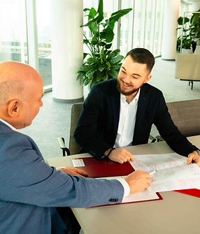 Joachim Kreutz zeigt mit einem Kugelschreiber auf einen Plan, während Nemanja Jovanovic ihn anblickt und lacht – Besprechungsszene bei JK Building Protection