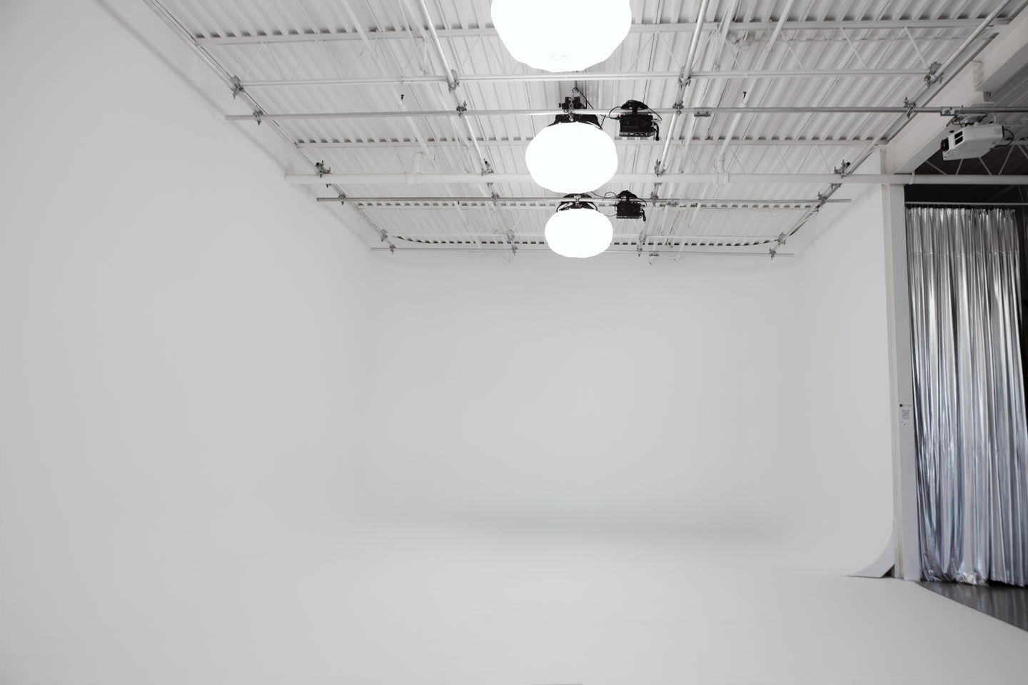 J-shaped white cyclorama with overhead soft orb lights and a silver curtain at the studio entrance.