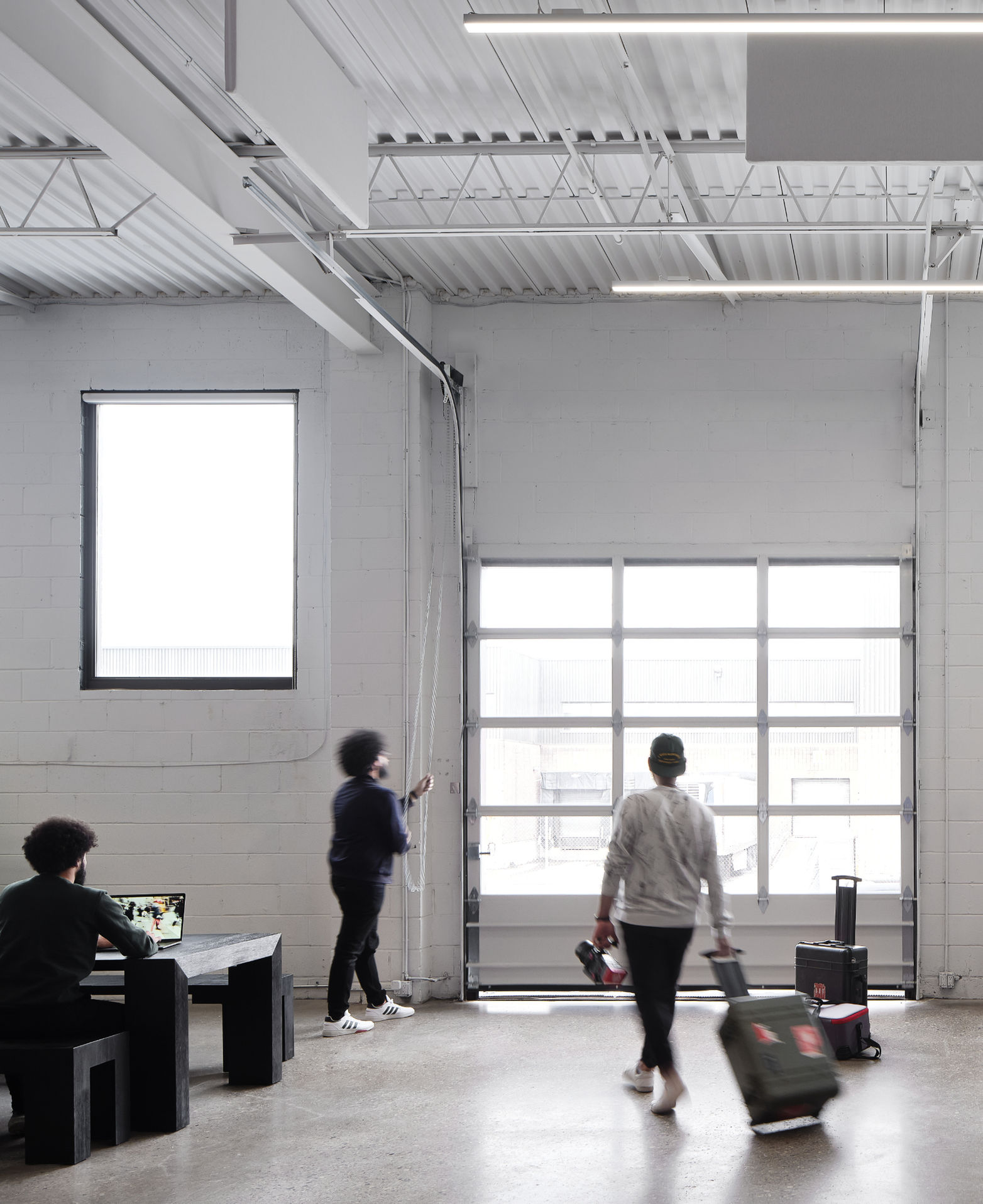 Crew working and loading gear near large windows and a glass garage door inside a bright studio space.