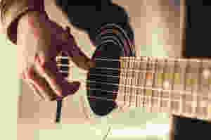 Right hand of a guitarist playing the strings of an acoustic guitar