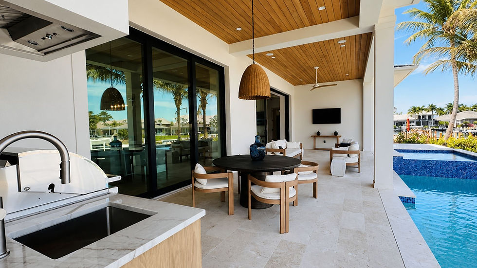 Luxury tropical patio with outdoor kitchen, round table and lounge chairs beside a blue pool, palm reflections, and TV.