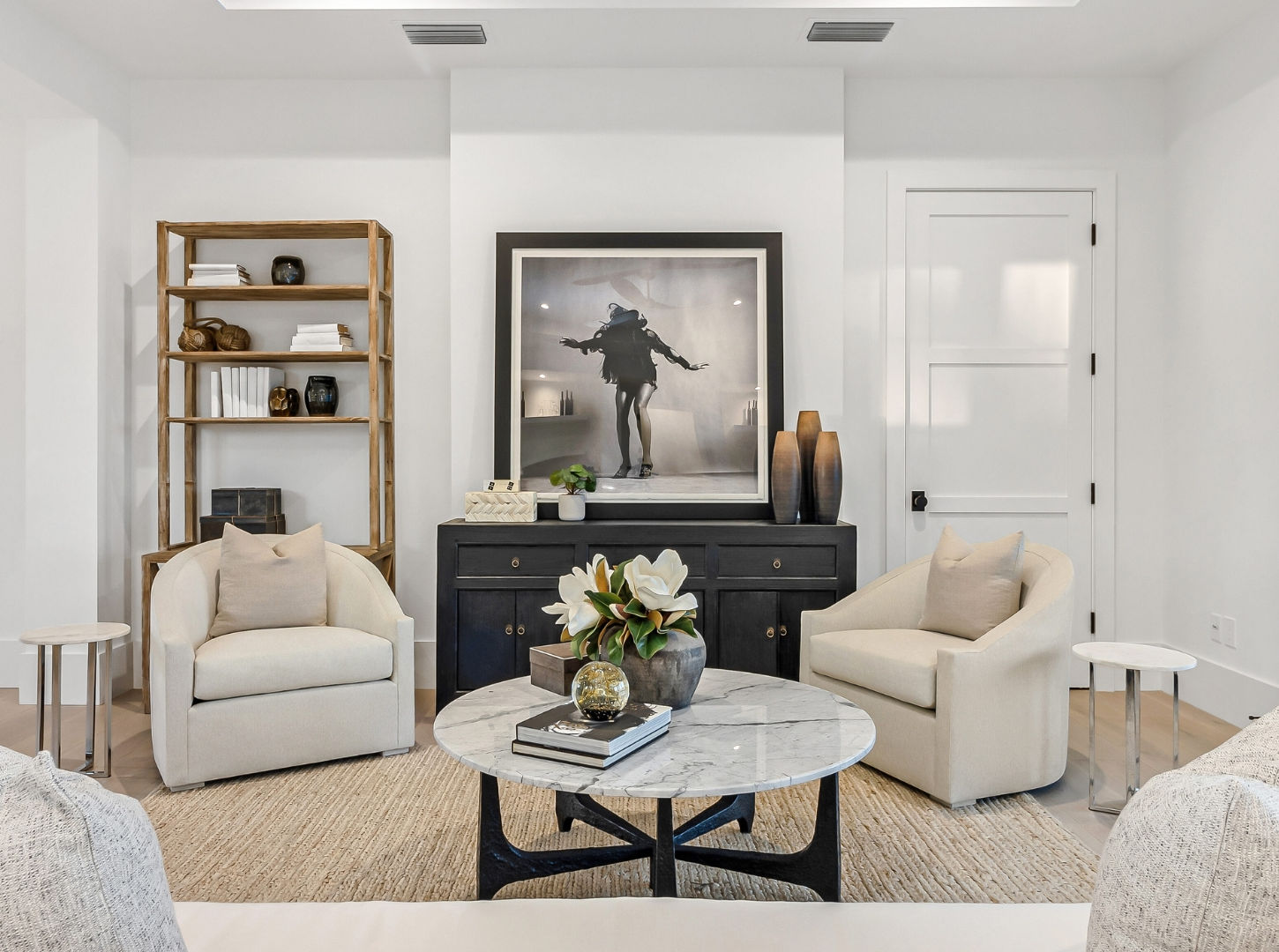 Conversation room with cream lounge chairs, a marble coffee table, black console, sculptural shelving, and sliding glass doors opening to a balcony.