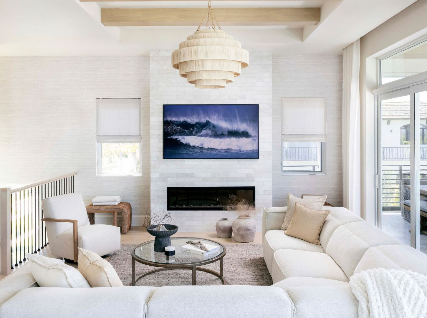 Living room with white sectional seating, a tiled fireplace wall, woven chandelier, neutral furnishings, and sliding glass doors opening to a balcony.