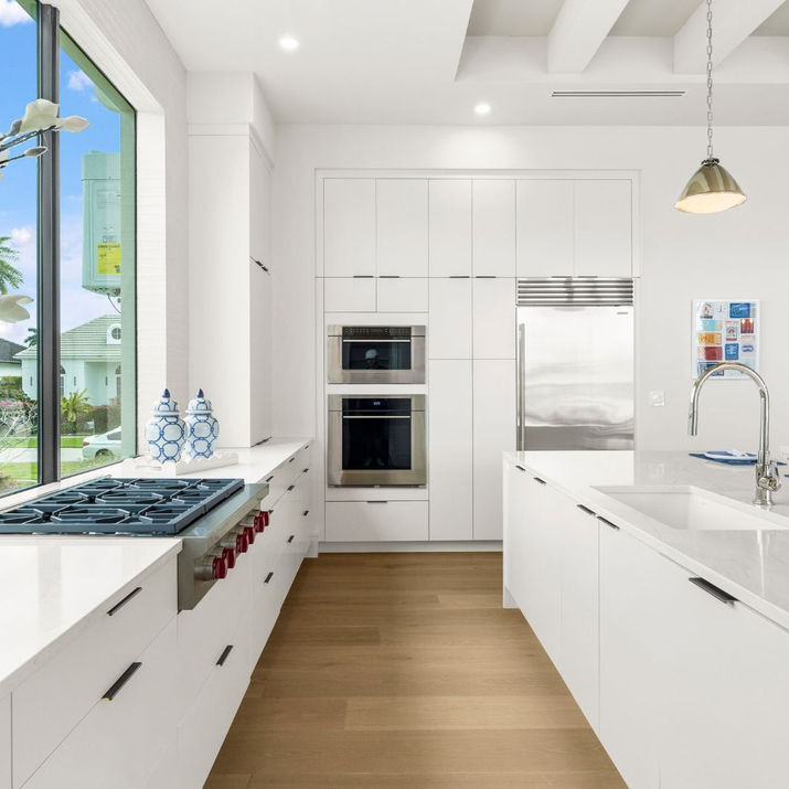 Modern white kitchen with a large island and garden view.