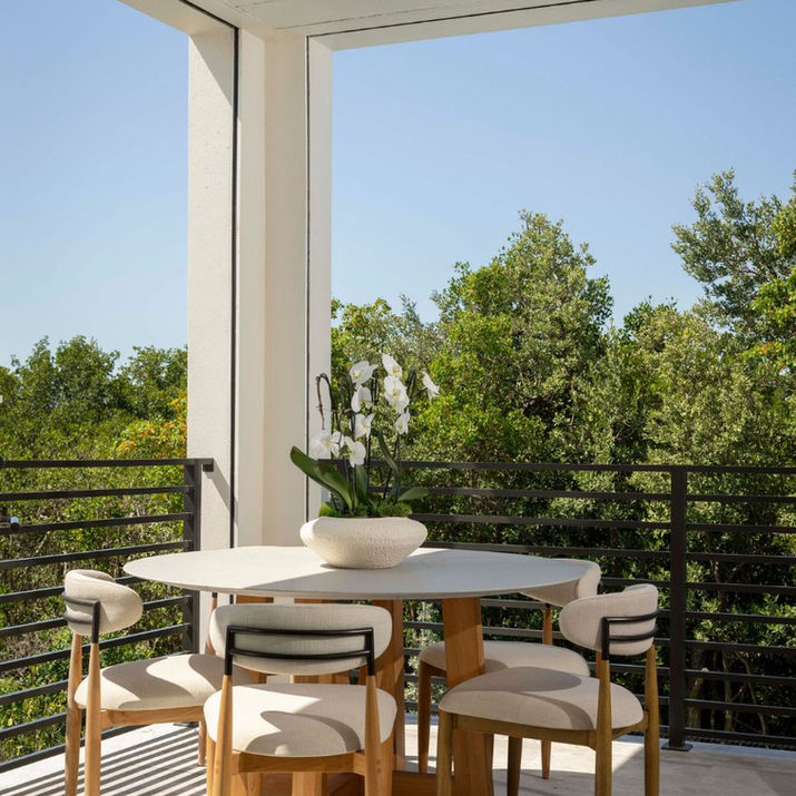 Covered lanai with a round dining table, upholstered chairs, black railings, and views of lush tropical greenery.