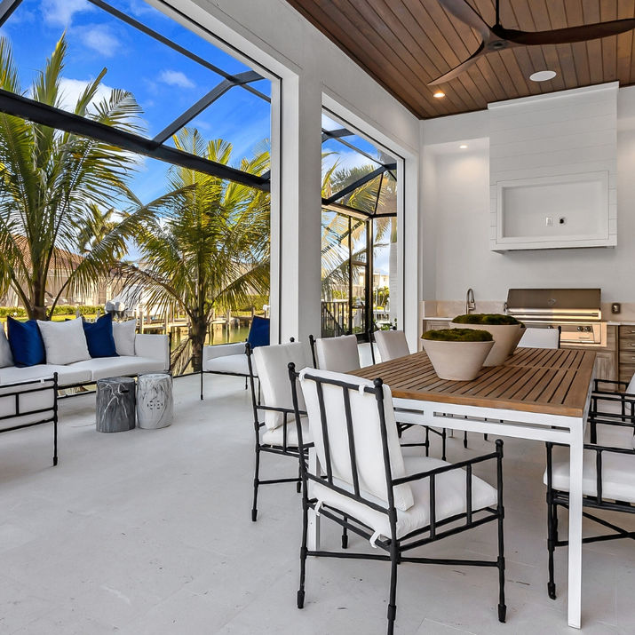 Covered lanai with outdoor dining, lounge seating, an outdoor kitchen, wood ceiling detail, and screened waterfront views.