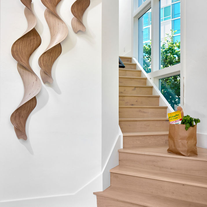 Staircase with light wood treads, large windows, sculptural wood wall art, and a grocery bag on the landing.