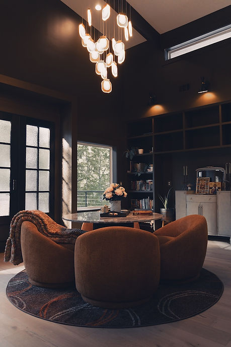 Moody modern home library interior design in Canton, GA, featuring custom dark charcoal built-in bookshelves, terracotta barrel chairs, and a round marble table by Reynard Architectural Designs .