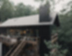 Exterior view of a multi-story black modern cabin featuring expansive wooden decks on multiple level