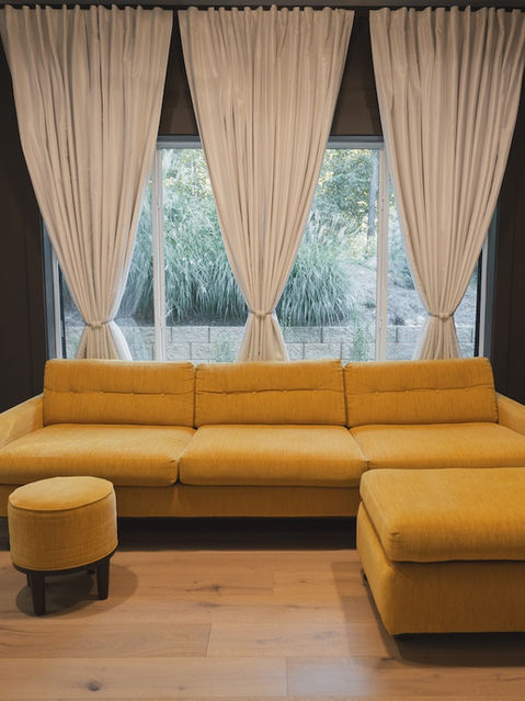 Dark painted room featuring a bright yellow mid-century style sofa and ottoman placed in front of a large window dressed with white tied-back curtains, flanked by two small hanging glass pendant lights.
Architecture by James Knight Photo by Kalyn Kight Reynard Architectural Designs