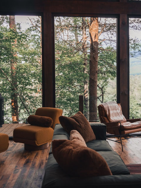 Comfortable armchairs and a modern black wood stove positioned next to large glass windows with a scenic view of green trees and distant mountains. Architecture by James Knight Photography by Kalyn Kight. Reynard Architectural Designs