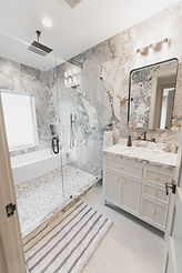 Luxury primary bathroom layout featuring a fluted light wood vanity, a black wall-mounted faucet, and a freestanding soaking tub enclosed by custom dark marble shower tiling.