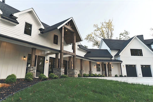 Exterior view of the Winding Ridge modern farmhouse in Blairsville, featuring white siding, black window frames, and a grand timber-framed entrance. Reynard Architectural Designs. Architect James Knight