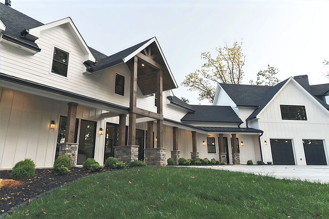 Photo of the front entrance of a custom home designed by architect James Knight. White board and batten siding with dark shingles and a two car garage. Timber columns and architectural details with green grass and stacked stone. Winding Ridge in Blairsville, GA is located in the private gated community of Highland Park in Blairsville, GA