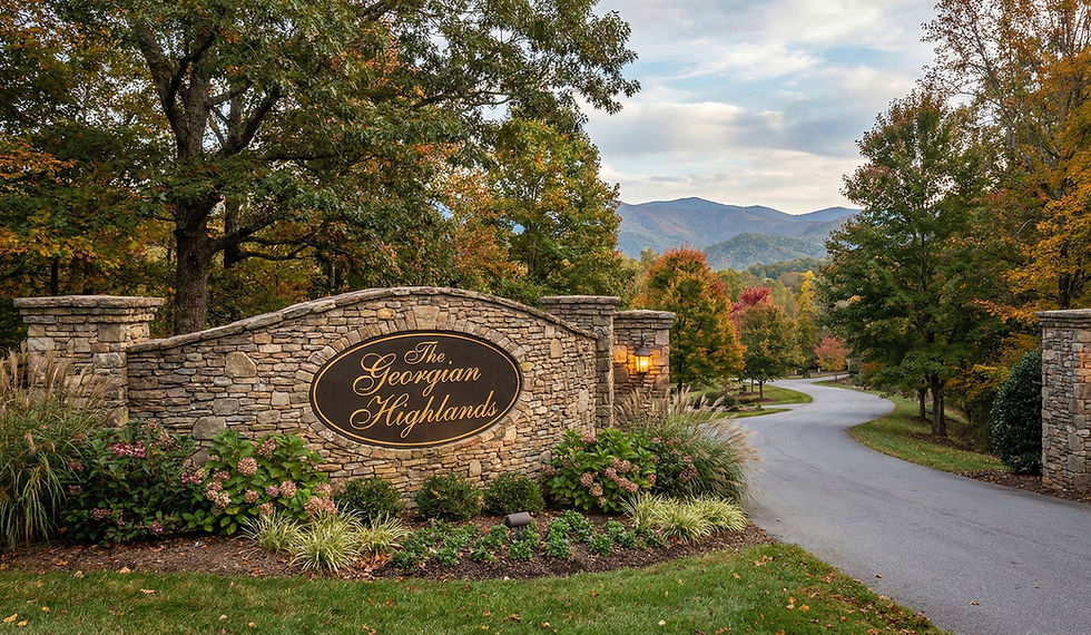 A stone community entrance monument featuring a central black oval sign with gold script lettering that reads "The Georgian Highlands." The sign is set into a stacked stone wall with columns, surrounded by manicured green shrubs and yellow bushes, with a backdrop of dense, tall forest trees. The Georgian Highlands - Reynard Custom Homes. North Georgia architect.