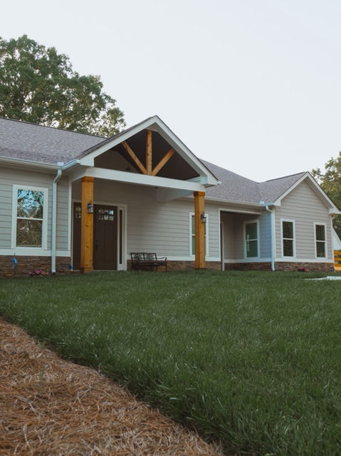 Wide exterior shot of a grey ranch-style house with a stone foundation, wooden front porch columns, and a manicured green lawn. Architecture by James Knight. Photo by Kalyn Kight