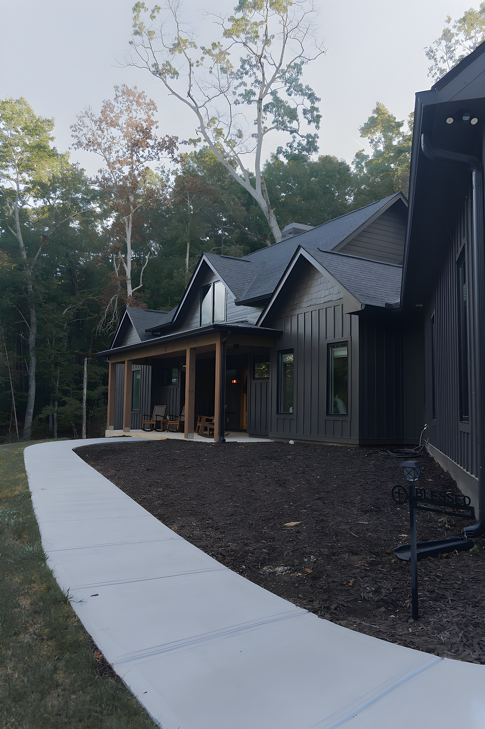 Front facade of a dark modern farmhouse named Redfield with a wide covered porch, wooden columns, and a black mailbox in the grassy foreground. Architecture by James Knight. Photo by Kalyn Kight. Mountain modern farmhouse by Reynard Architectural Designs