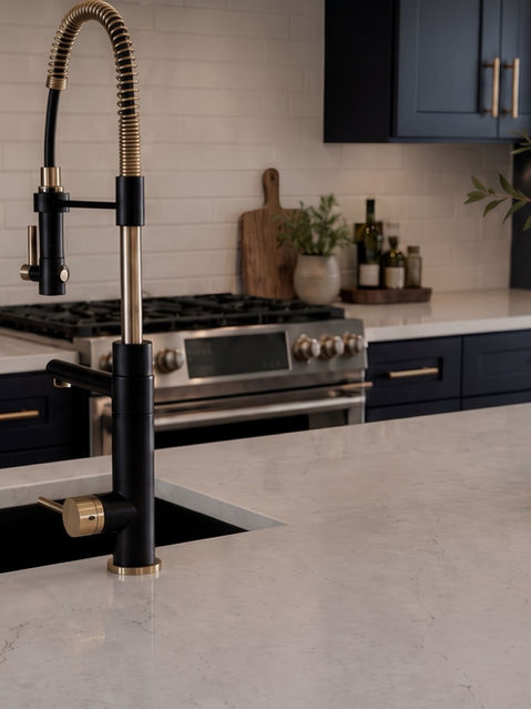 Close-up of a matte black and gold pull-down spring faucet on a white quartz kitchen island with navy blue cabinetry and white subway tile in the background. Talking Rock, GA Reynard Architectural Designs