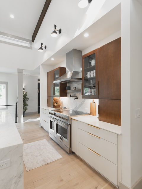 Bright modern kitchen with a vaulted ceiling, dark wood beams, white marble island, stainless steel appliances, and a mix of dark wood and white cabinetry.